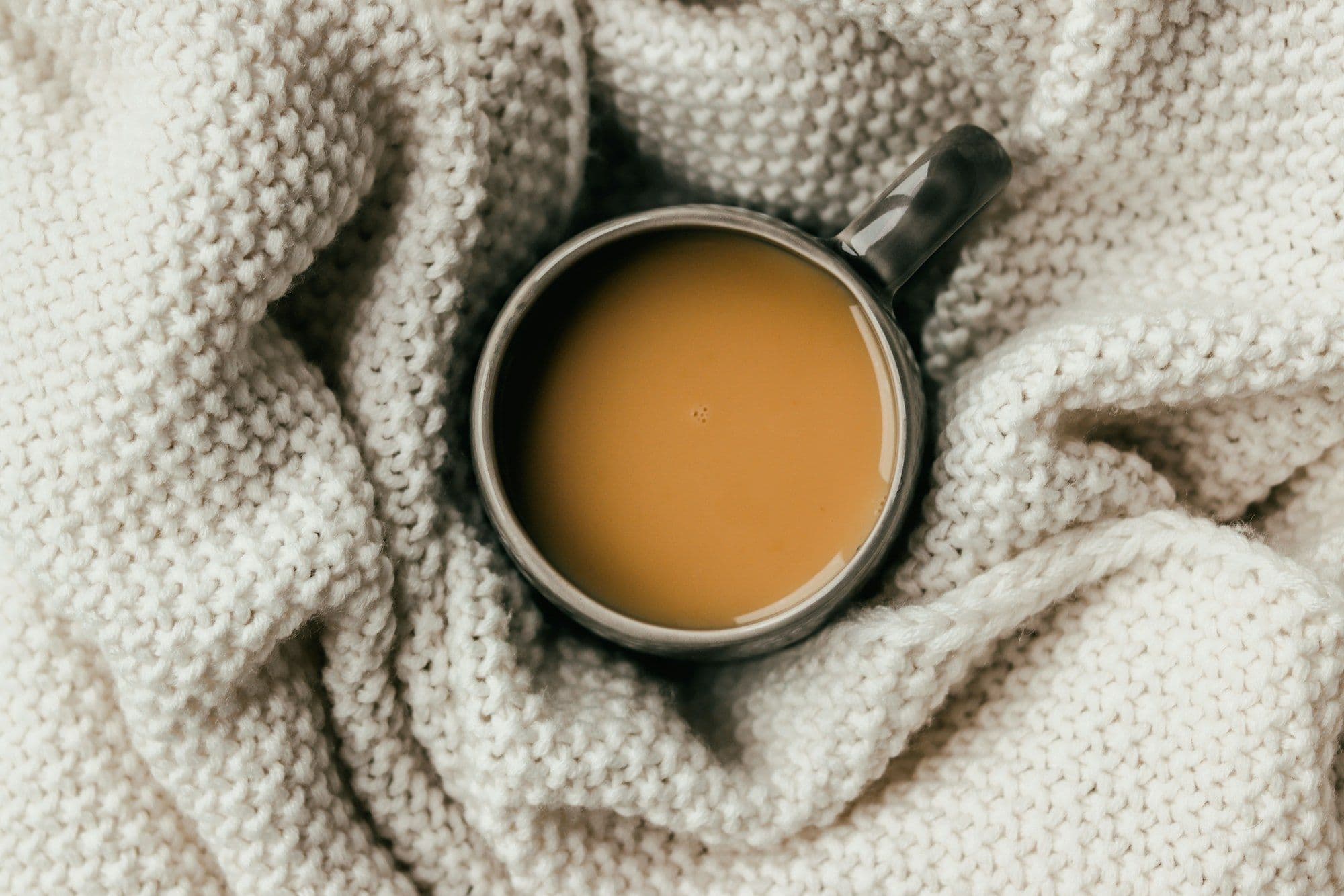 A warm drink resting on a soft cream knit blanket